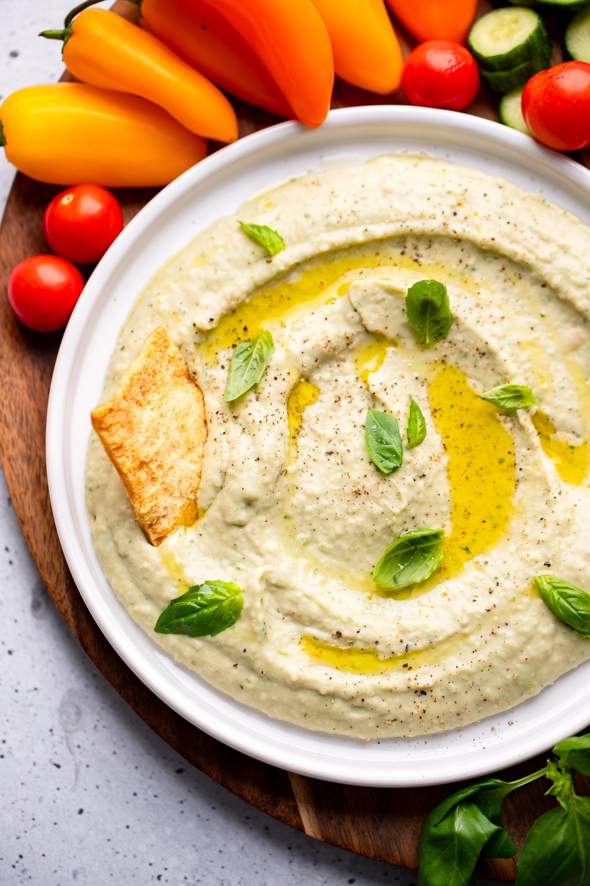 Near the immersion of the white bean in a white bowl surrounded by vegetables and cookies.