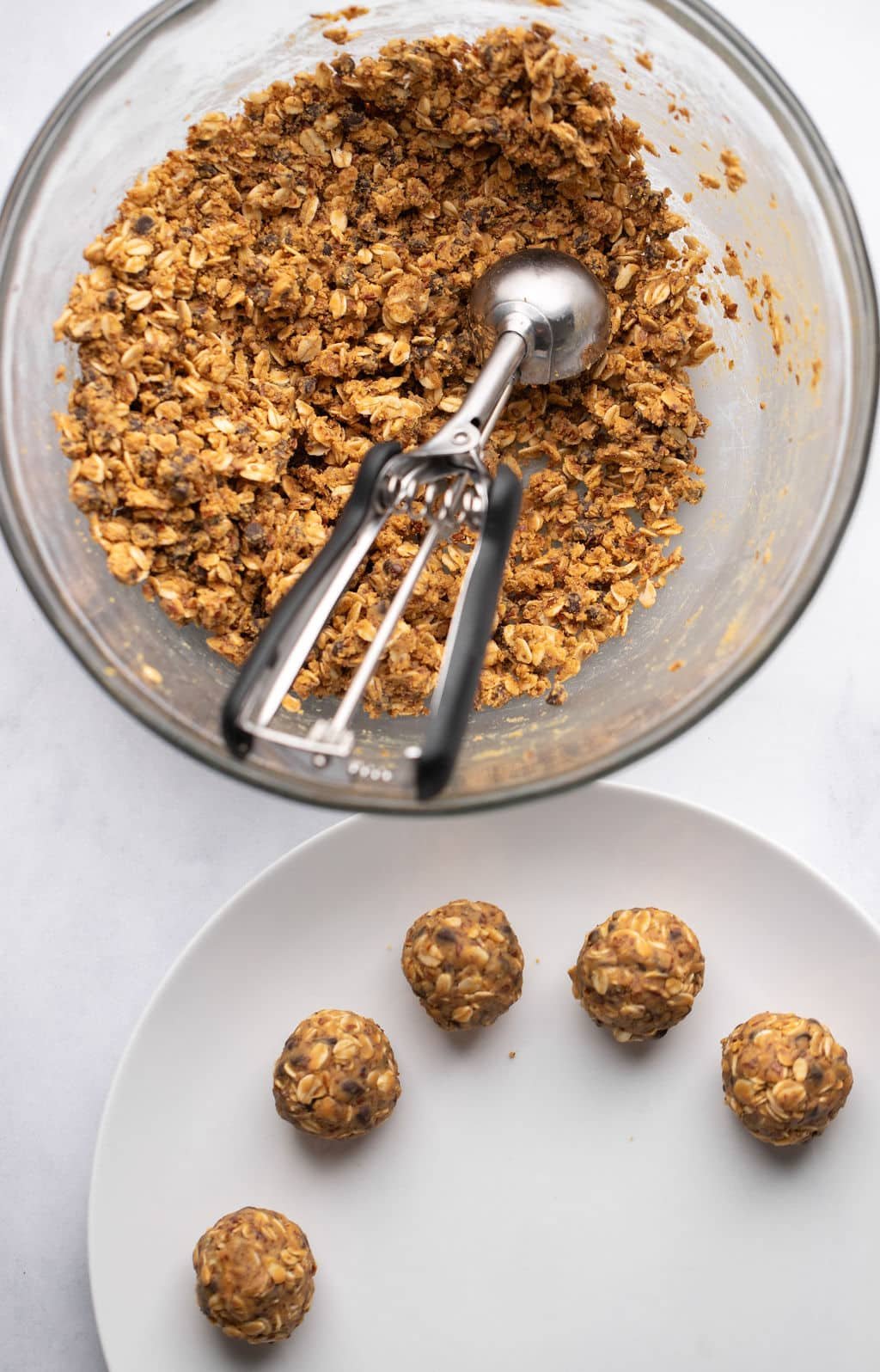 A glass bowl with a mixture of oatmeal butter next to peanut butter energy balls rolled on a white plate.