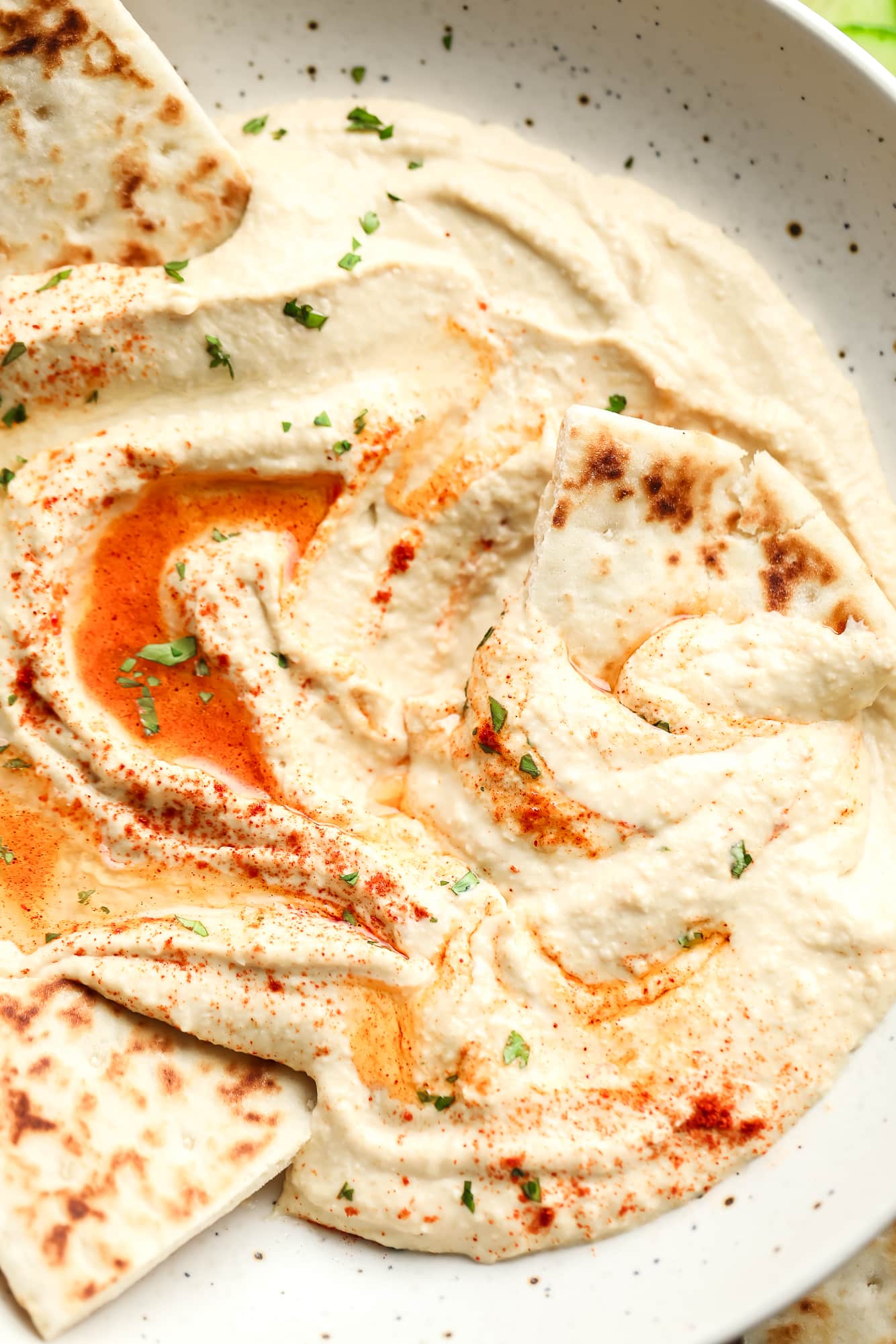 Hummus topped with paprika and oil in a white bowl with pita bread on the side.