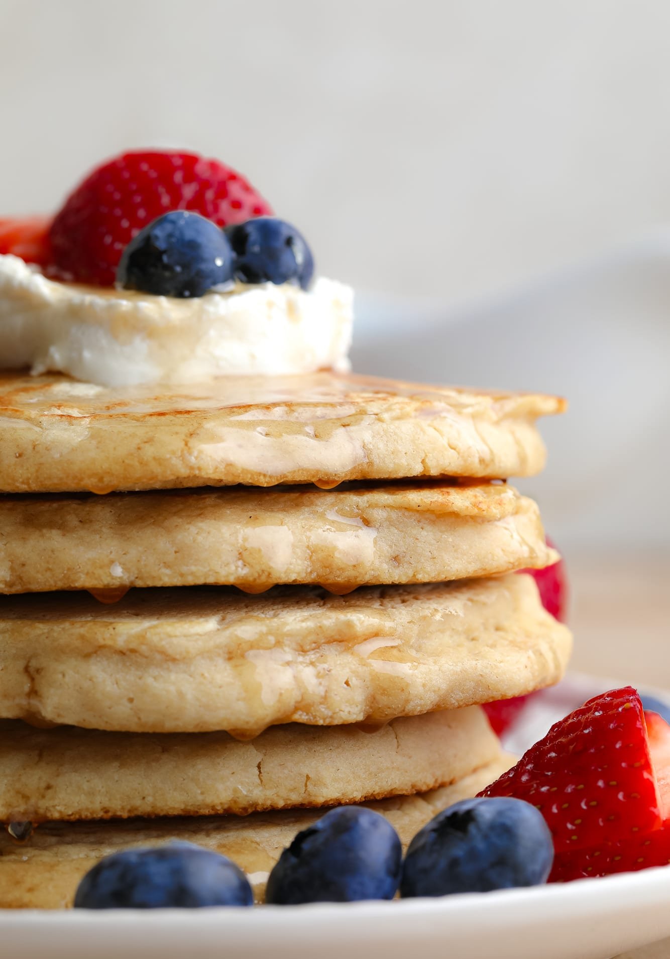 Near a pile of vegan oatmeal pancakes with butter and berries on top.