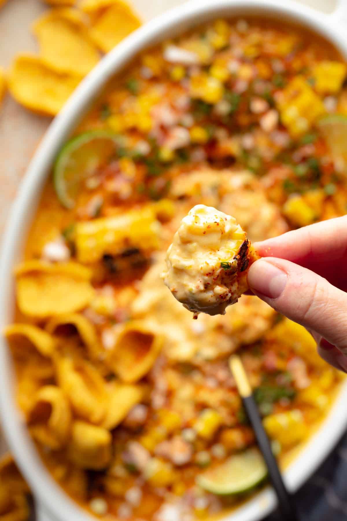 The hand of the woman who holds a chip of corn with a spoon of mexican vegan corn.